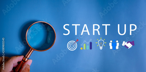Hand holding magnifying glass with Start Up text and business strategy icons