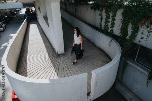 Schilderij op canvas Senior business woman walks alone on a curved concrete ramp wearing professional clothing and sunglasses