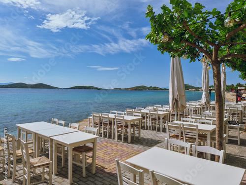 Canvas Print View of the mediterranean sea with Greek restaurant tables and blue turquoise se