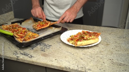 Homemade vegetable pizza with chicken is served from a baking sheet to a plate in the kitchen.