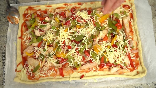 Close-up of homemade pizza preparation with tomato sauce, cheese, chicken, and colorful bell peppers before baking.