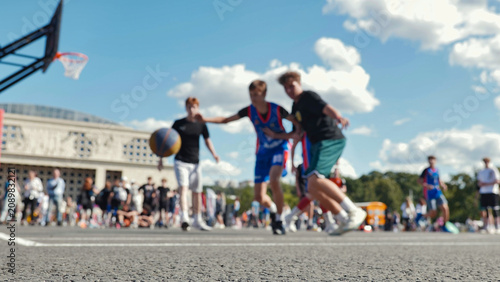 Asphalt basketball court with blurred players in action on a sunny day.