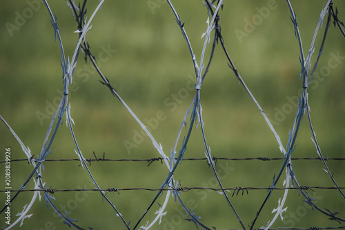 Fotografie Barbed wire fence with sharp spikes and twisted strands, set against a blurred g