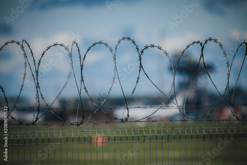 Slika na platnu Barbed wire fence with twisted strands in focus, blurred background showing indu