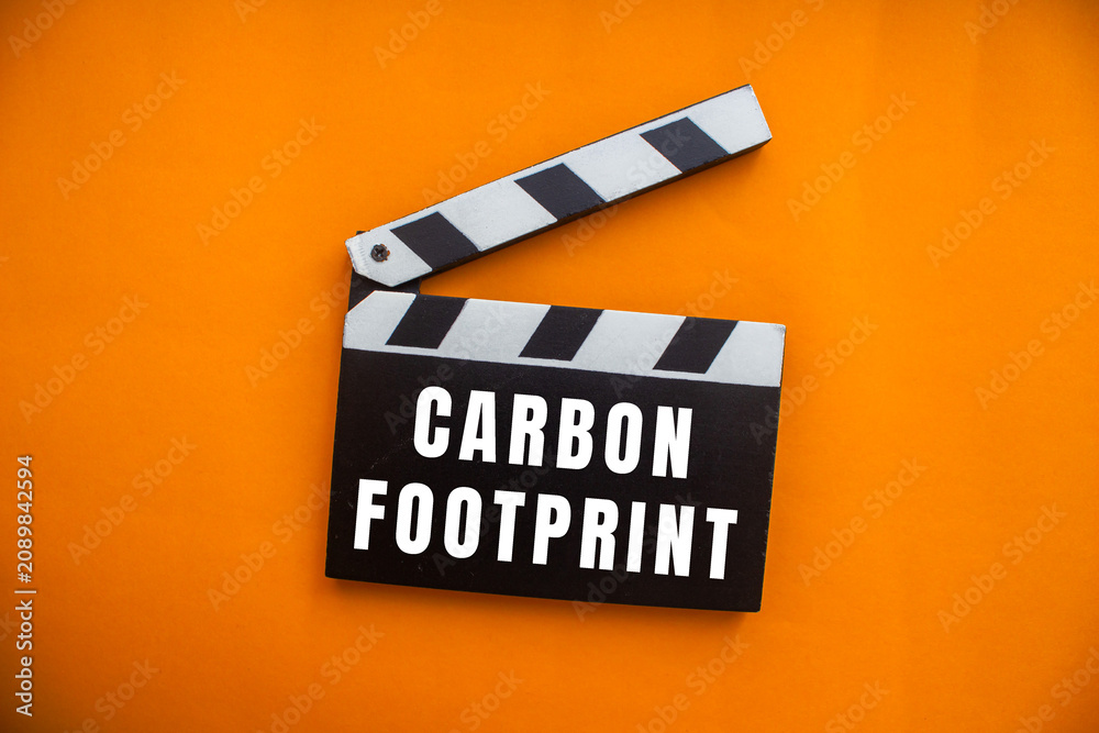 Naklejka premium Clapperboard displaying carbon footprint against an orange background, symbolizing environmental impact and sustainability in cinema