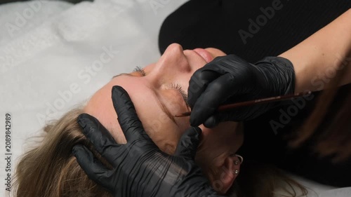 Professional cosmetologist applying permanent makeup to a client's eyebrow in a beauty salon