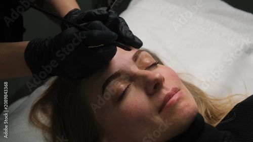 Professional cosmetologist coloring client's eyebrows with a brush during a permanent makeup procedure
