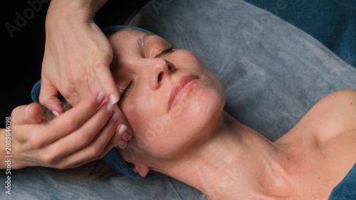 Relaxed middle-aged woman receiving an anti-aging facial massage treatment from a beautician