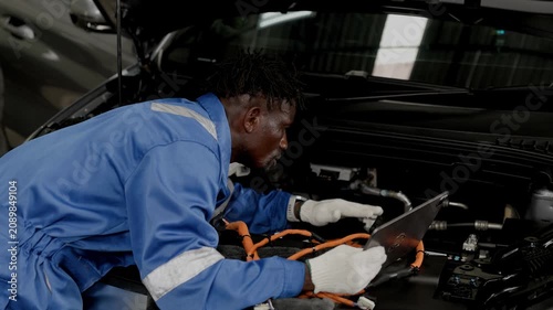 Professional African black male worker working service maintenance EV car in EV garage auto workshop, Cabling DC Inverter power line.