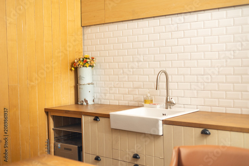 Stylish kitchen interior with a deep white sink, natural wooden cabinetry, white subway tiles, and a decorative flower arrangement creating a clean and inviting atmosphere.