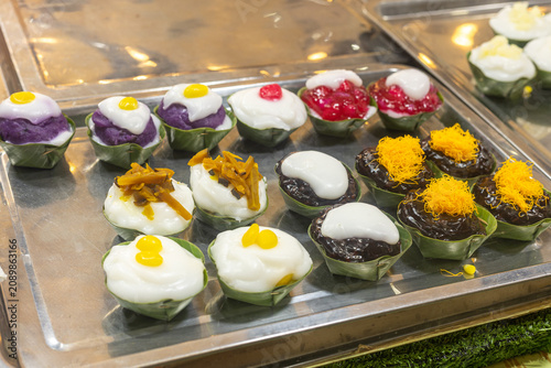 Assorted Thai Tako desserts beautifully arranged on a stainless steel serving tray, featuring colorful toppings on coconut cream in traditional banana leaf cups at a local dessert shop.