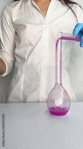 A person in a lab coat mixes different liquids in a lab setting while wearing gloves. The liquids change colors as they are combined step by step.