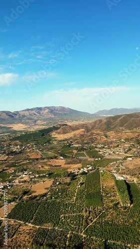 A wide view of Malaga Spain captures fields, mountains, and blue sky. The camera showcases the landscape from above with hills and farmland below.