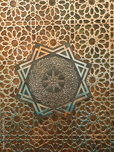 Detailed Arabic calligraphy carving in the shape of an eight-pointed star on a metal door or mosque wall.