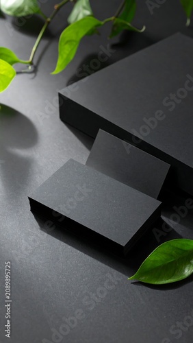 A close-up of matte black business cards on a dark surface with green leaves