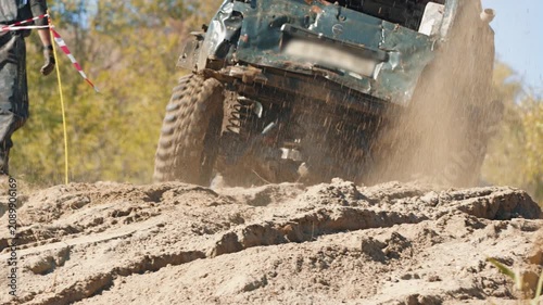 Action shot of modified car competing in off road race. Vehicle speeds up sandy hill, kicking up large cloud of dust and dirt. Bright daylight illuminates dynamic scene