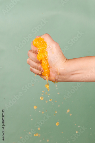 Foto Fresh Mandarin Orange Segment Being Squeezed in Hand with Juice Dripping Against