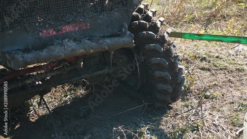 A close-up of a massive off-road tire with a muddy rim that has come off. The car sits with a flat tire on rough terrain during an extreme motorsports competition