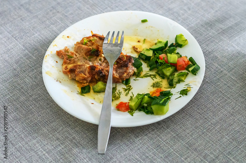 Fotografie Partially eaten meal with roasted meat, fresh salad and fork on white plate