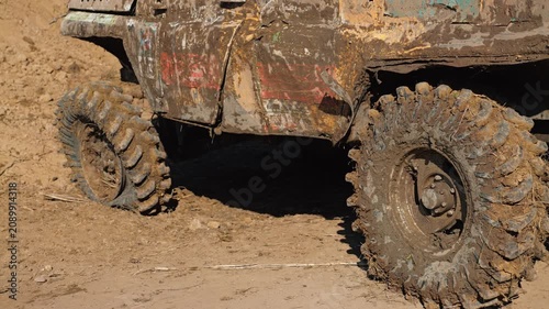 Close up view of massive muddy tire on custom off road truck. Vehicle is covered in dirt after extreme competition. Bright sunlight creates strong shadows. Adventure and motorsports concept