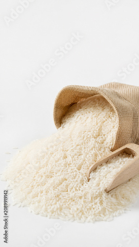 Unveiling a bounty of grains, a burlap sack spills its contents of white rice, a wooden scoop nestled amongst the pile, hinting at culinary preparation.