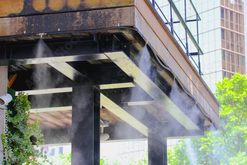 Outdoor mist cooling system spraying water fog under a building terrace to cool down a hot summer day.
