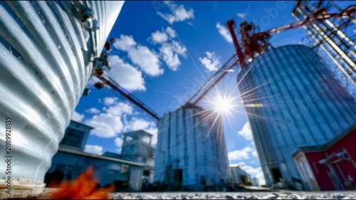 Industrial grain silos under bright blue sky, agricultural storage facility with metal towers, cranes, sunlight and rural production concept