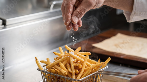 Julienne fries hand salt basket kitchen julienne fries in metal basket with chef hand adding salt over hot crispy potato snack in professional kitchen