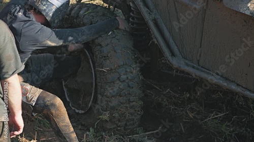 The co-pilot repairs a mud-stained SUV after a breakdown. A man is trying to put a loose tire on a disc. Teamwork and challenge in motorsport