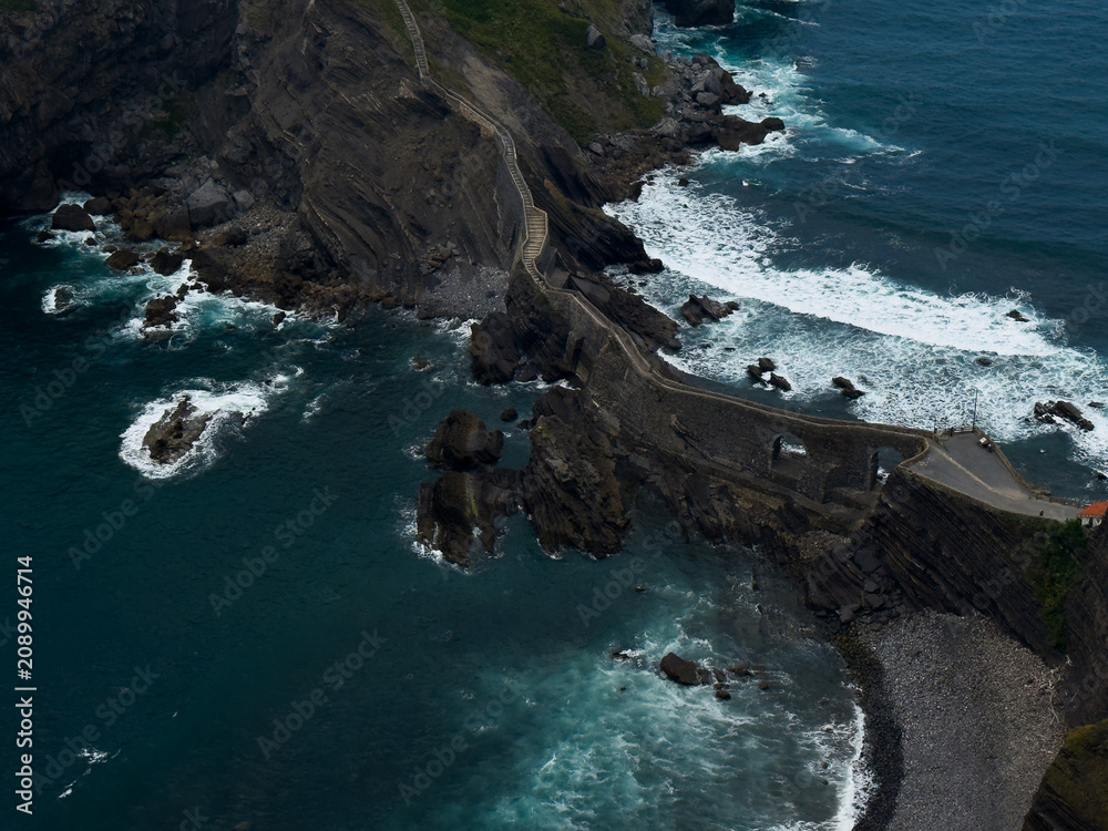 Naklejka premium winding pathway along rocky cliffs by ocean with rugged and adventurous atmosphere. aerial perspective highlights natural beauty and adventure in travel and outdoor settings.