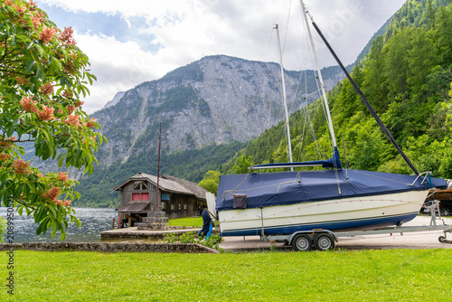 Foto Sailing boat on a trailer by a wooden boathouse with alpine mountain and bloomin
