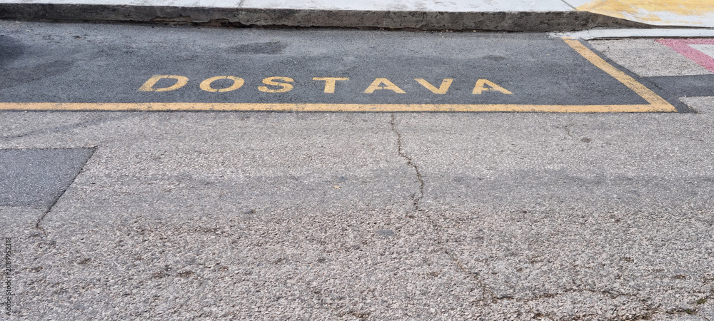 Fototapeta premium A yellow parking zone designated for delivery vehicles with the Croatian word DOSTAVA painted on the street asphalt.