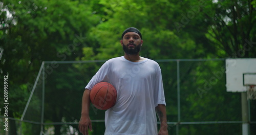 Canvas Print African American man holding basketball under arm on outdoor court, steady gaze