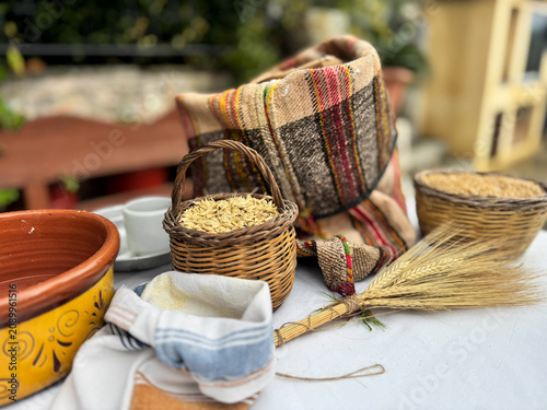 Traditional outdoor still life featuring ancient zea grains and wheat in woven baskets, a vintage woven sack and flour. Ideal for authentic heritage, baking and Mediterranean diet themes. Empty space.