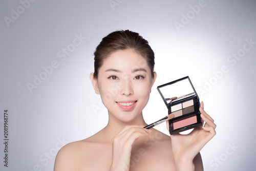 Fotografie Smiling young woman holding eyeshadow palette and makeup brush