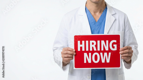 Healthcare professional holding hiring now sign in modern medical setting