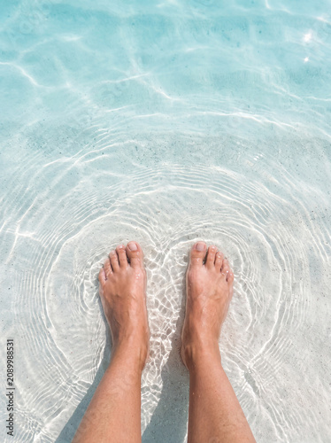 Bare feet in crystal clear shallow tropical water with gentle ripples and white sand
