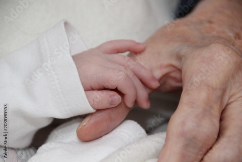 Close-up of the wrinkled hands of an older woman holding the tiny hand of a newborn baby
