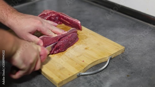 Horizontal 4K video close up. Male hand cutting piece of fresh raw juicy beef meat with knife on wooden cutting board on kitchen table. Concept of healthy food, preparing dinner, lunch, no vegan cafe