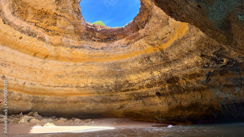 Exploring a cave along the coast with a round opening in the ceiling revealing blue sky, Portugal