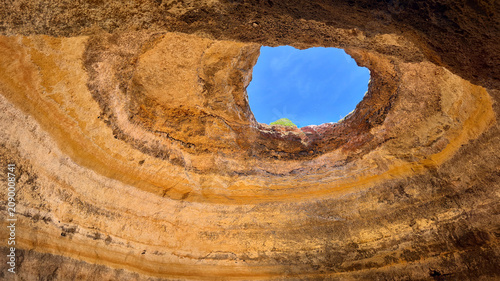 View of the inside of a large cave with a hole in the ceiling located in a natural area during daylight, Portugal