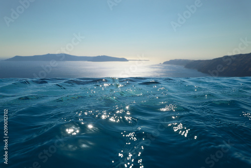 Infinity pool water merges seamlessly with the Aegean Sea as sunlight dances across gentle waves, framing Santorini’s volcanic islands in a serene, dreamlike Mediterranean horizon.