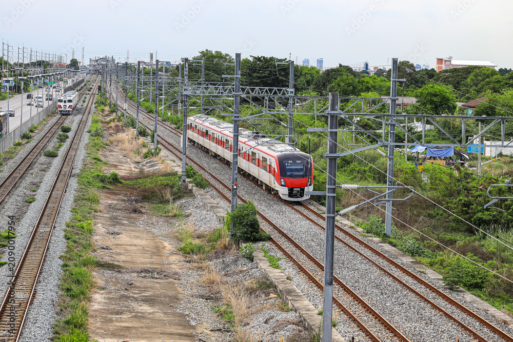 Obraz premium Red Commuter Train on the railroad tracks heading towards the City, outdoor landscape.
