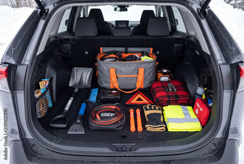 Inside the trunk of a vehicle, a winter car kit is organized with tools and supplies for emergency situations during winter weather. Items include a shovel, blankets, and safety gear