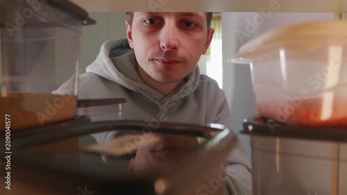 Young man looking for grain containers inside a kitchen cupboard