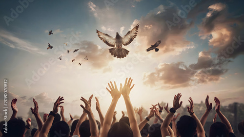 A large crowd of people with their hands raised towards the sky as a flock of doves flies upward into a bright, golden sunset with clouds