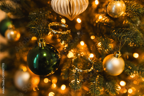 Canvastavla Close up of golden and green glass balls hanging on a Christmas tree with warm bokeh lights