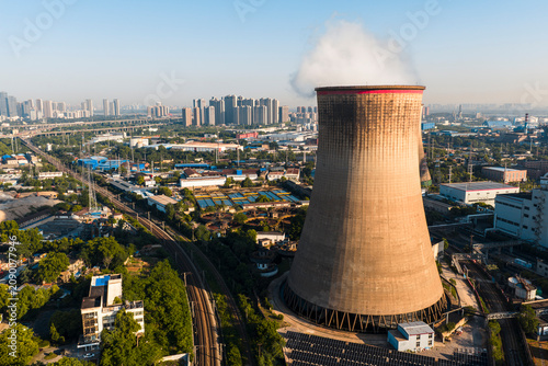 Obraz na plátně Aerial view of a chinese nuclear power plant cooling tower emitting steam near a modern city, featuring surrounding industrial railways and solar panels at sunrise