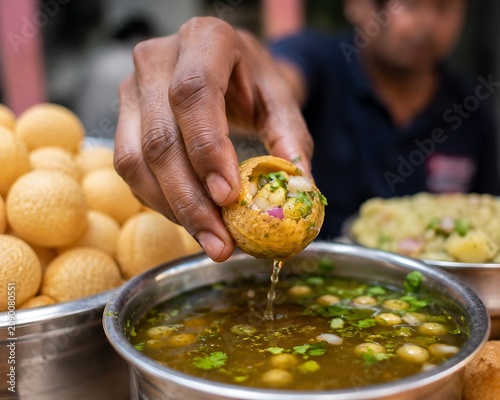 Freshly cracked fuchka being filled with spicy potato mixture and dipped into flavored tamarind water, action food photography, detailed textures, realistic street food scene.