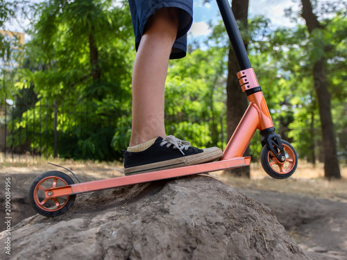 Slika na platnu A boy stands with his feet on a stunt scooter stuck in a dirt hill in the park